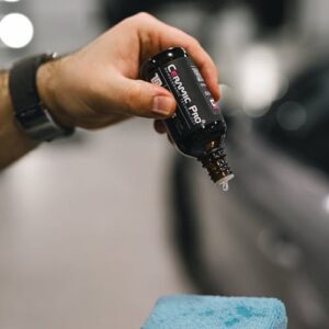 Hands applying ceramic coating to car surface with blue sponge
