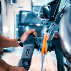 Detailer using electric buffer with orange polishing pad on car paint
